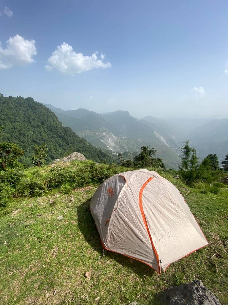 A tent on a grassy ridge above a forested valley