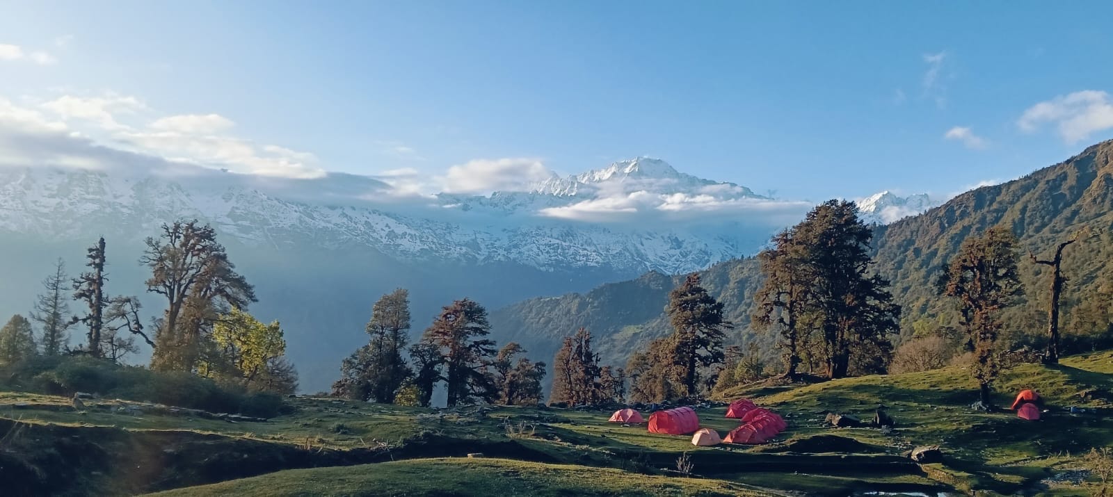 Snowy peaks rising above a high meadow with tents and pine trees